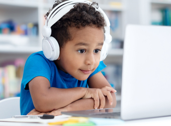 Child intently watches and listens to his laptop during his virtual tutoring session at home.